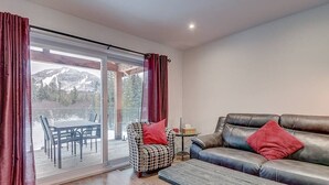 Un salon comprenant un canapé, un fauteuil, une table basse et donnant sur une terrasse avec une table et des chaises.