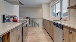 Une cuisine moderne avec des meubles en bois, une hotte de cuisine en acier inoxydable et une grande fenêtre offrant une vue sur l’extérieur.