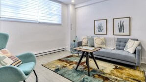 Ein modernes Wohnzimmer mit einem grauen Sofa, einem blauen Sessel und einem Couchtisch. An der Wand befinden sich zwei gerahmte Pflanzenbilder.
