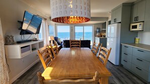 Een moderne keuken met een eethoek, een aan de muur bevestigde televisie en uitzicht op de oceaan.