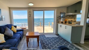 Een woonkamer met een blauwe bank, een houten salontafel en uitzicht op de oceaan door grote glazen schuifdeuren.