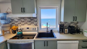 Een keuken met uitzicht op de oceaan, een waterdispenser, een waterkoker, een koffiezetapparaat en een vaatwasser.