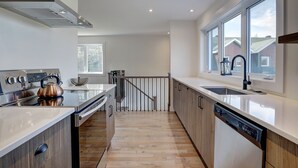 Une cuisine moderne dotée d’appareils électroménagers en acier inoxydable, de planchers en bois et de grandes fenêtres offrant une vue sur le quartier.