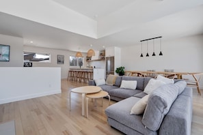 Uma sala de estar moderna com sofá cinza, mesa de centro de madeira e luminárias pendentes.