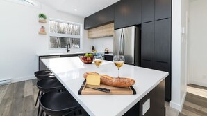 A modern kitchen with a large island, dark cabinets, and a stainless steel refrigerator. - Hôtel à la maison - Le Quintessence, spa et vue (Saint-Irénée)