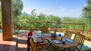 Un espace de restauration en plein air avec une table et des chaises en bois, un mur en pierre et une vue sur les arbres et les montagnes.