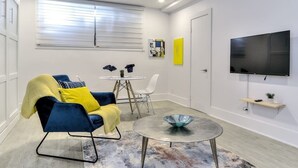 Un salon moderne avec un canapé bleu, une petite table ronde et un téléviseur fixé au mur.