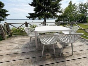 Une terrasse en bois avec une table et des chaises blanches, donnant sur une étendue d’eau.