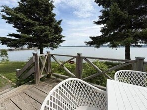 A wooden deck with white lattice chairs and a view of a lake.