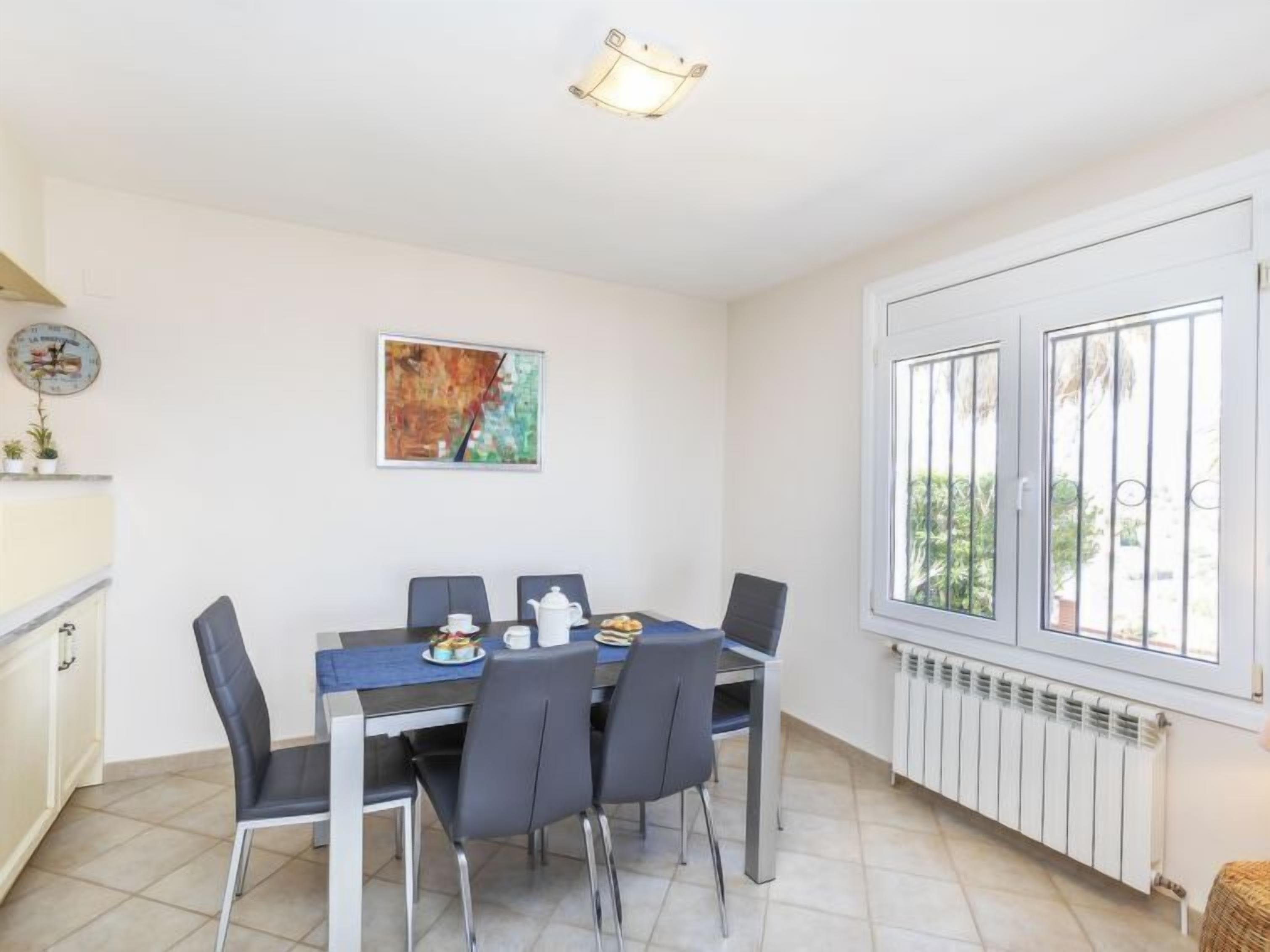 Ein Essbereich mit Tisch für vier Personen, Stühlen, einem Bild an der Wand und einem Fenster mit Gitterstäben.