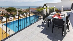 Eine Dachterrasse mit Swimmingpool, Essbereich im Freien und Blick auf Stadt und Meer.