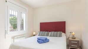 Ein Schlafzimmer mit einem Bett, einem Fenster, einem Nachttisch und einer Lampe.