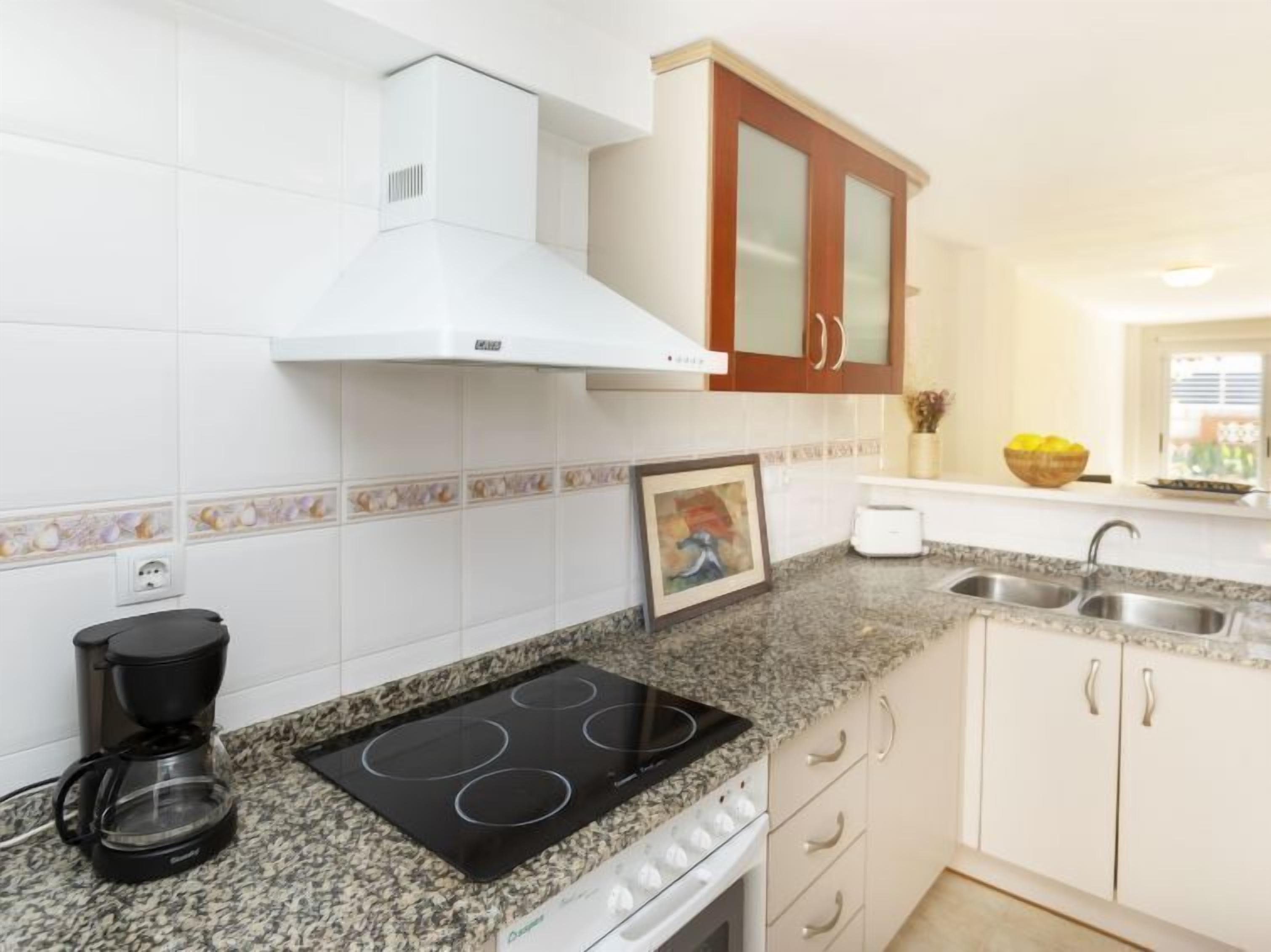 Eine Küche mit weißen Schränken, einer schwarzen Induktionskochplatte, einer Kaffeemaschine und einem Toaster.