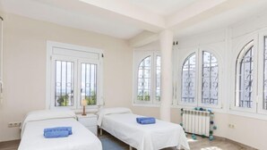 Ein Zimmer mit zwei Betten, einem Heizkörper und großen Fenstern mit Metallgitter.