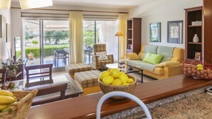 A modern living room with a sofa, a coffee table, and a dining area with chairs and a table. There is a large window with curtains, a bookshelf, and a hanging light fixture. - Gabriel by Interhome (Sant Jordi)