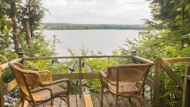 A wooden deck with wicker chairs overlooking a lake.