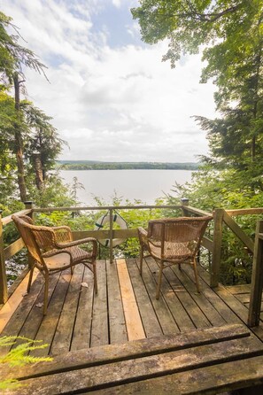 Una terraza de madera con sillas de mimbre con vistas a un lago.