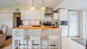 A modern kitchen with white cabinetry, a wooden island, and white chairs. There is a stove, oven, and refrigerator.