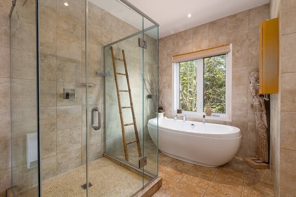 Ein modernes Badezimmer mit einer gläsernen Duschkabine, einer freistehenden Badewanne und einem Fenster, das für natürliches Licht sorgt.
