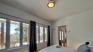 Un dormitorio con un ventanal grande, una cama con ropa de cama a rayas y una lámpara en el techo.