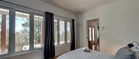 A bedroom with a large window, a bed with striped bedding, and a ceiling light.