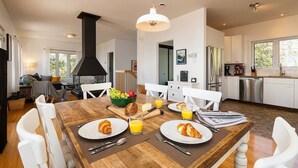 Una cocina moderna con armarios blancos, electrodomésticos de acero inoxidable y un comedor con mesa de madera dispuesta para el desayuno.