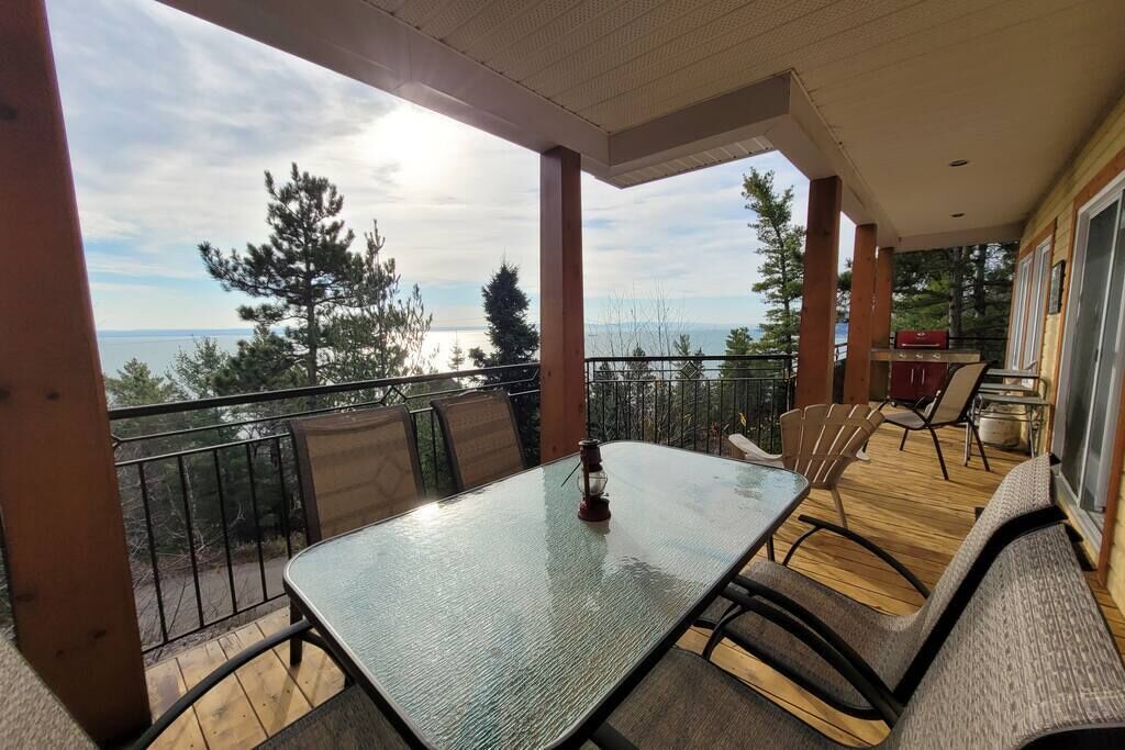 A balcony with a table and chairs, overlooking a body of water and trees.