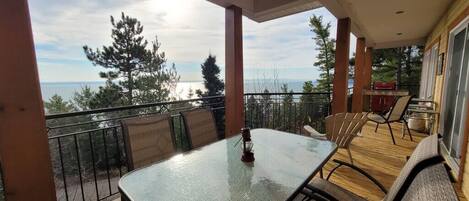 A balcony with a table and chairs, overlooking a body of water and trees.