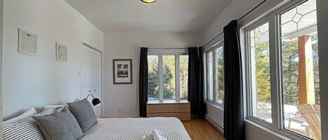 A bedroom with a bed, a bedside table, a window with curtains, and a view of trees outside.
