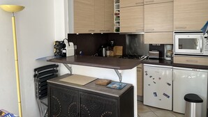 A modern kitchen with wooden cabinets, a built-in microwave, a coffee machine, and a small refrigerator. - Pontaillac 30m Plage 1er Étage Villa (Royan)