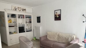 A living room with a sofa, two armchairs, a coffee table, a bookshelf, and a dartboard. - Pontaillac 30m Plage 1er Étage Villa (Royan)