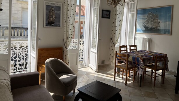 A living room with a sofa, armchair, dining table with chairs, a chandelier, and a painting of a ship. - Pontaillac 30m Plage 1er Étage Villa (Royan)