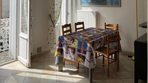 A dining area with a table covered in a colorful tablecloth, wooden chairs, a chandelier, a painting of a ship on the wall, and a radiator. - Pontaillac 30m Plage 1er Étage Villa (Royan)
