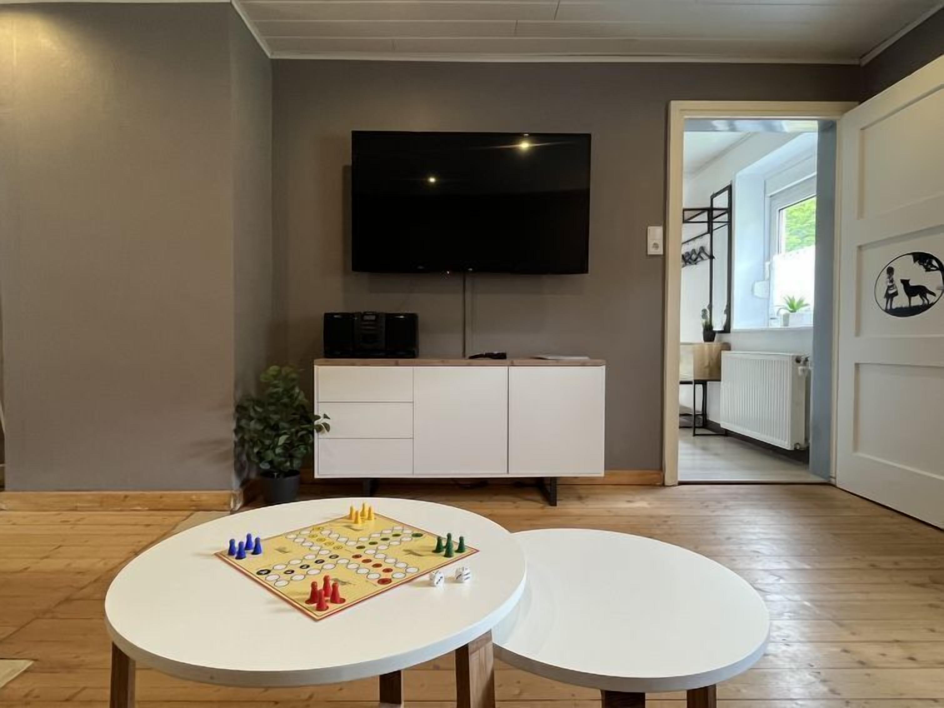 A room with a TV mounted on the wall, a white cabinet, two round tables, and a chessboard on one table.