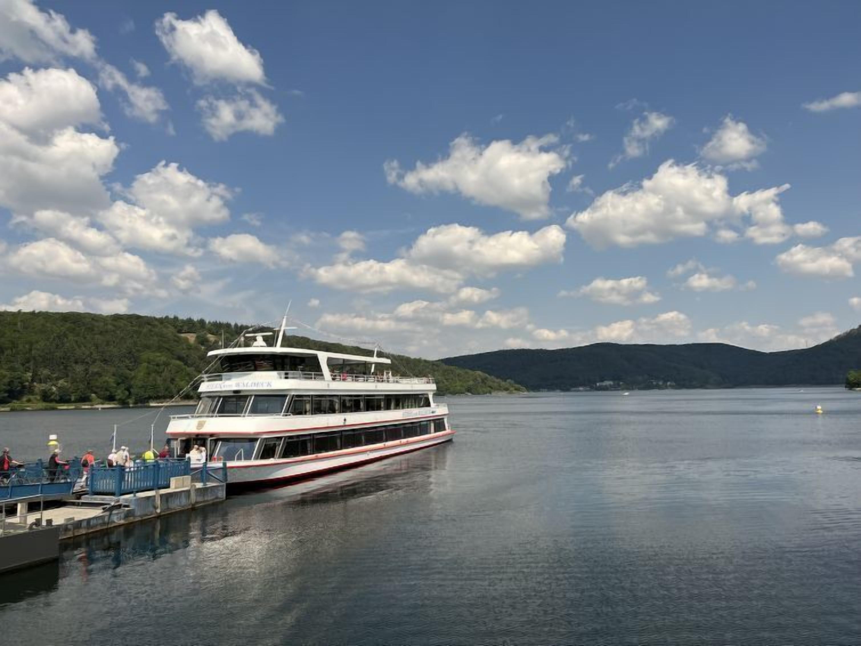 A white riverboat docked at a pier with passengers boarding.