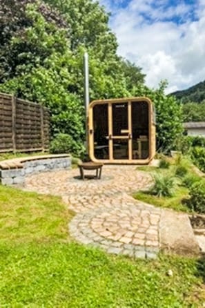 A garden with a stone pathway leading to a wooden structure with glass doors.