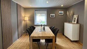 Un espace repas moderne avec une table en bois et des chaises noires, un meuble blanc agrémenté d’objets décoratifs et une fenêtre donnant sur un paysage verdoyant.