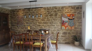 A dining area with a stone wall, wooden table, chairs, hanging pendant lights, and artwork.