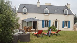 A two-story house with a patio area featuring wicker furniture, a table, and two red lounge chairs.