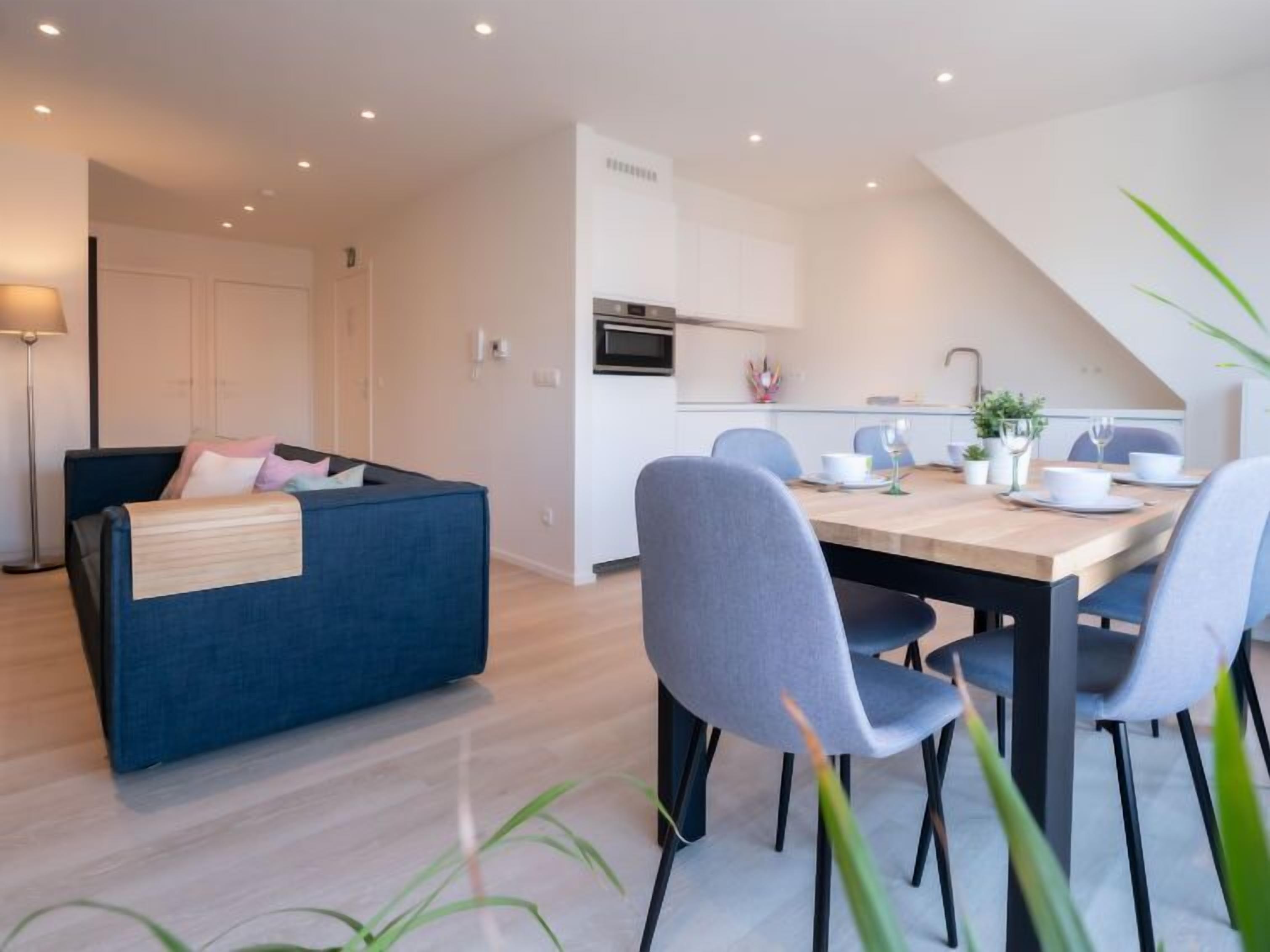 A modern living space with a sofa, dining table, chairs, and a kitchen area.