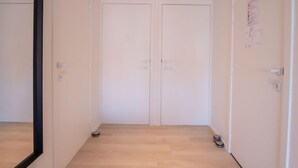 Um corredor com duas portas brancas, piso de madeira e uma pequena lixeira perto da porta direita.