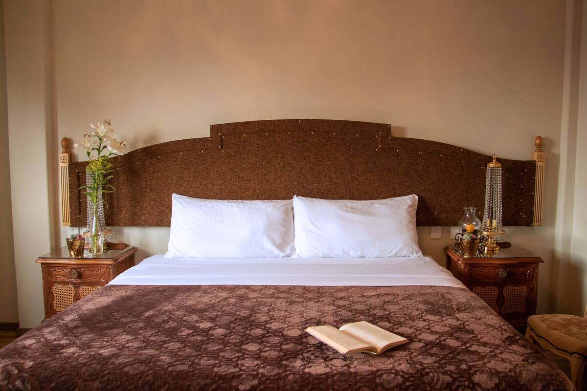 Una cama bien hecha con un edredón estampado, dos almohadas y un libro abierto sobre la cama.