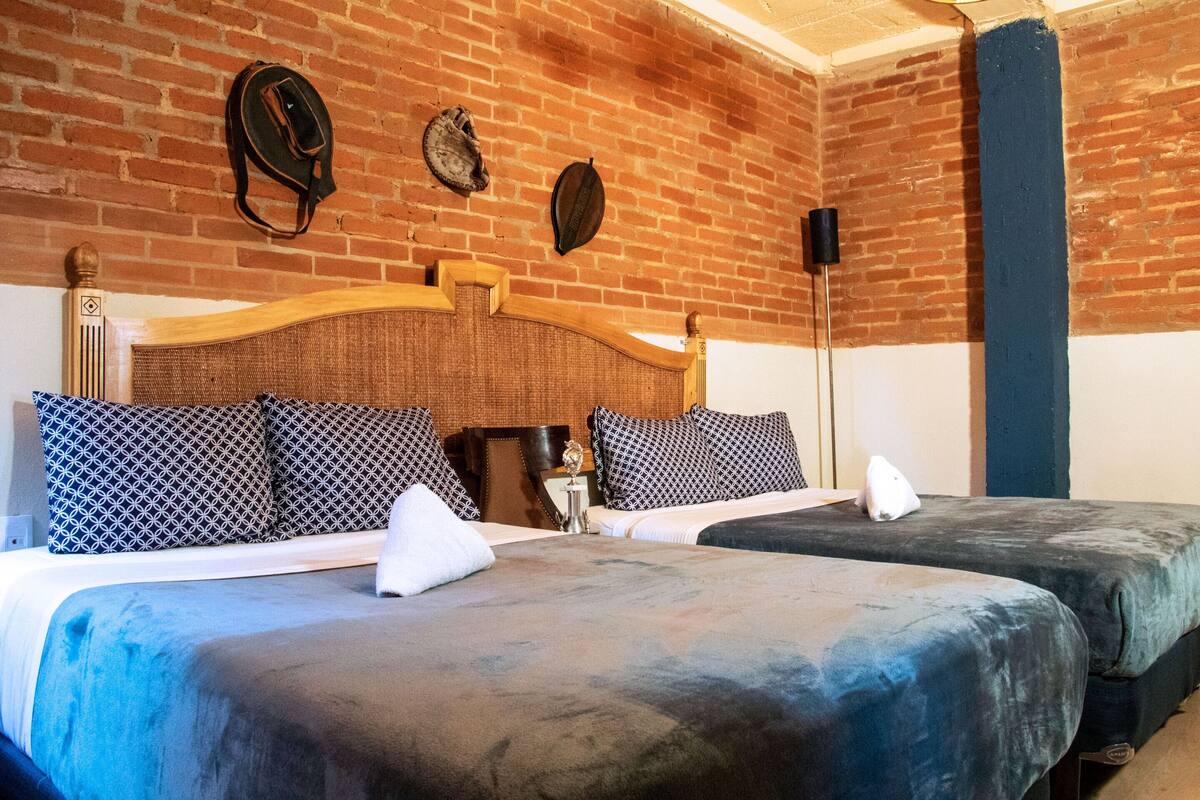 Una habitación con dos camas, un muro de ladrillo y un cabecero de madera.