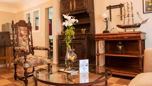 A room with a round glass table, a floral upholstered chair, a wooden cabinet, and a ship model on a shelf. - Antique Hotel (Mexico City)