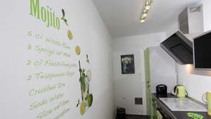 Eine Küche mit einer Tafel, auf der Zutaten für einen Mojito aufgelistet sind, einem grünen Wasserkocher, einer schwarzen Kaffeemaschine und einer grünen Tasse auf der Arbeitsfläche.