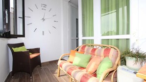 Ein Zimmer mit einem Korbssessel, einer Wanduhr, einem grünen Vorhang und einer Topfpflanze.