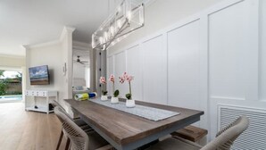 Un comedor con una mesa de madera, sillas de mimbre y una pared blanca con un televisor.