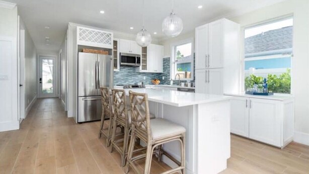 Una cocina moderna con armarios blancos, una isla central y taburetes de bar.