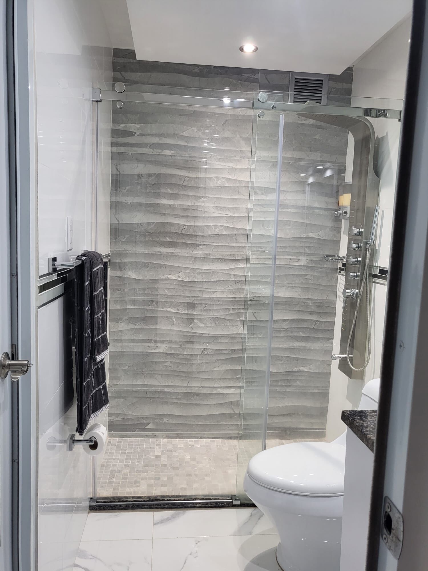 Une salle de bain moderne avec une douche à parois de verre, des toilettes blanches et un porte-serviettes avec une serviette noire.