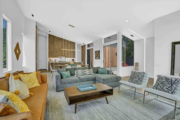 A modern living room with a sectional sofa, a coffee table, and a dining area with a wooden accent wall.